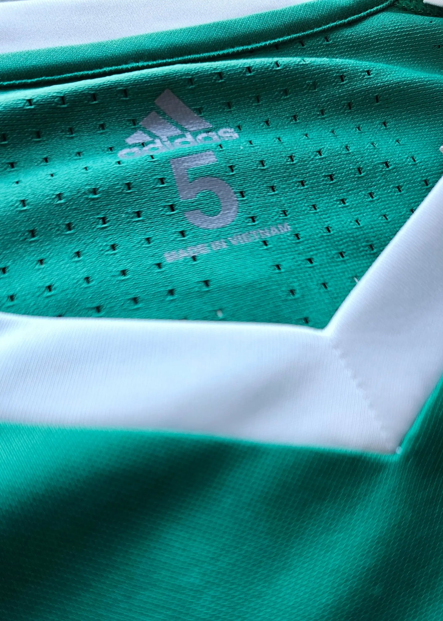 Close-up view of adidas logo and No. 5 on green football shirt with white accents.