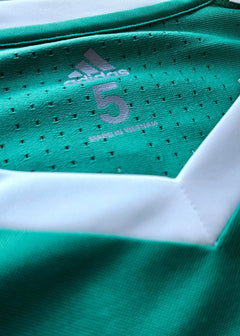 Close-up view of adidas logo and No. 5 on green football shirt with white accents.
