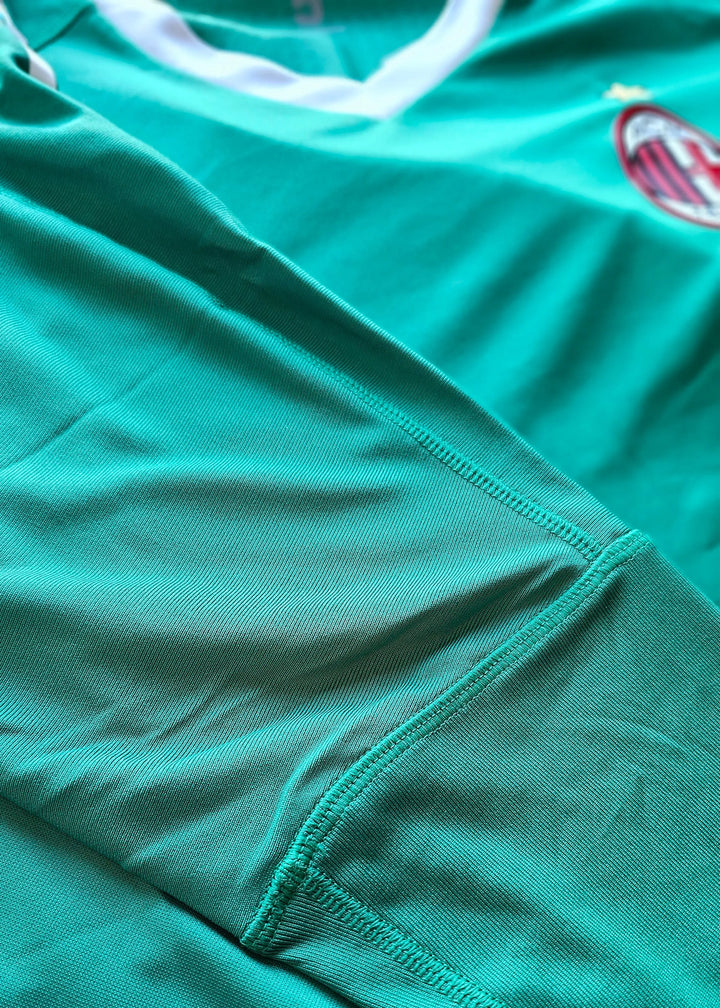 Close-up of the AC Milan crest on a signed soccer jersey in turquoise color.