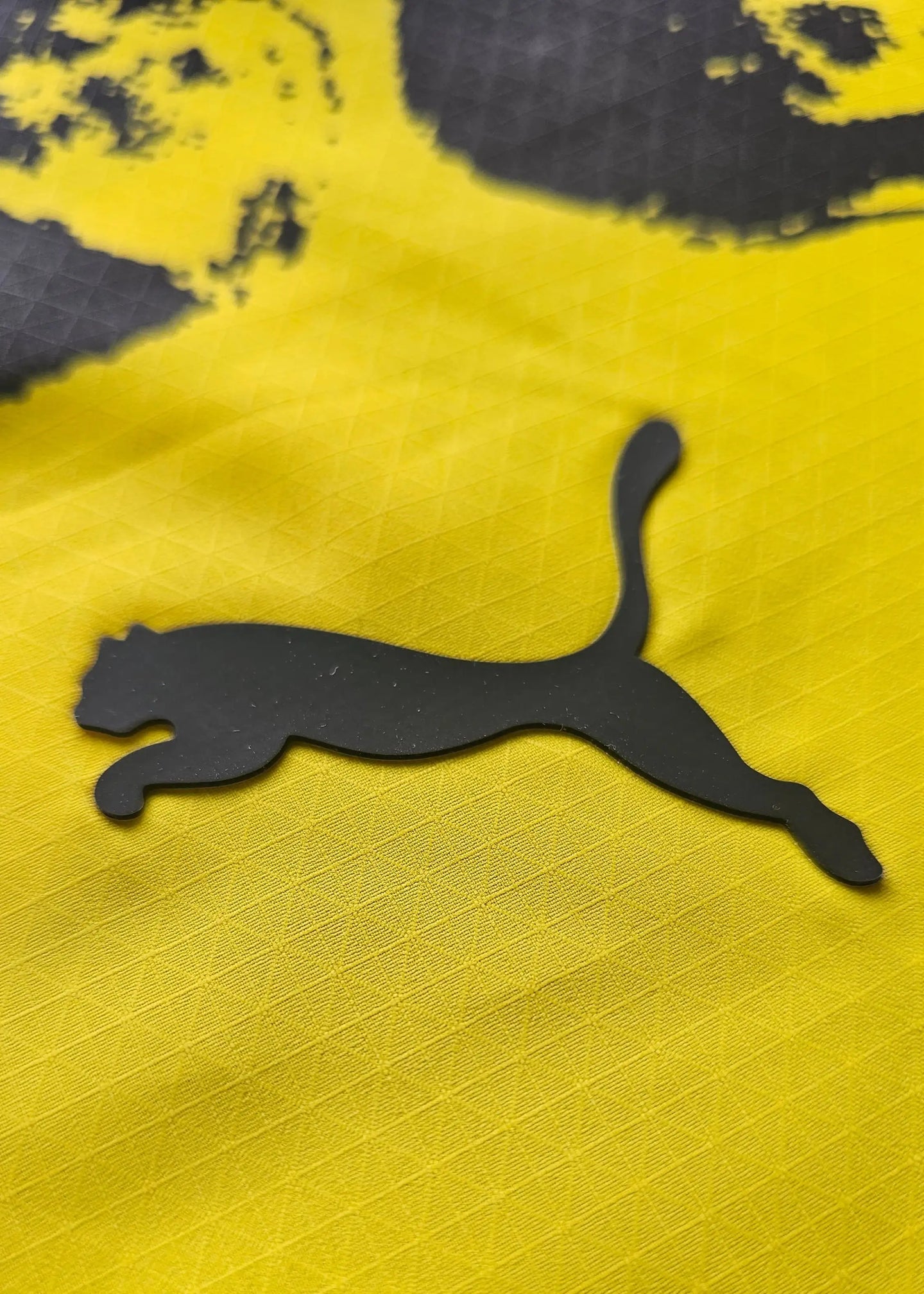 Close-up view of the black Puma logo on a yellow football shirt.