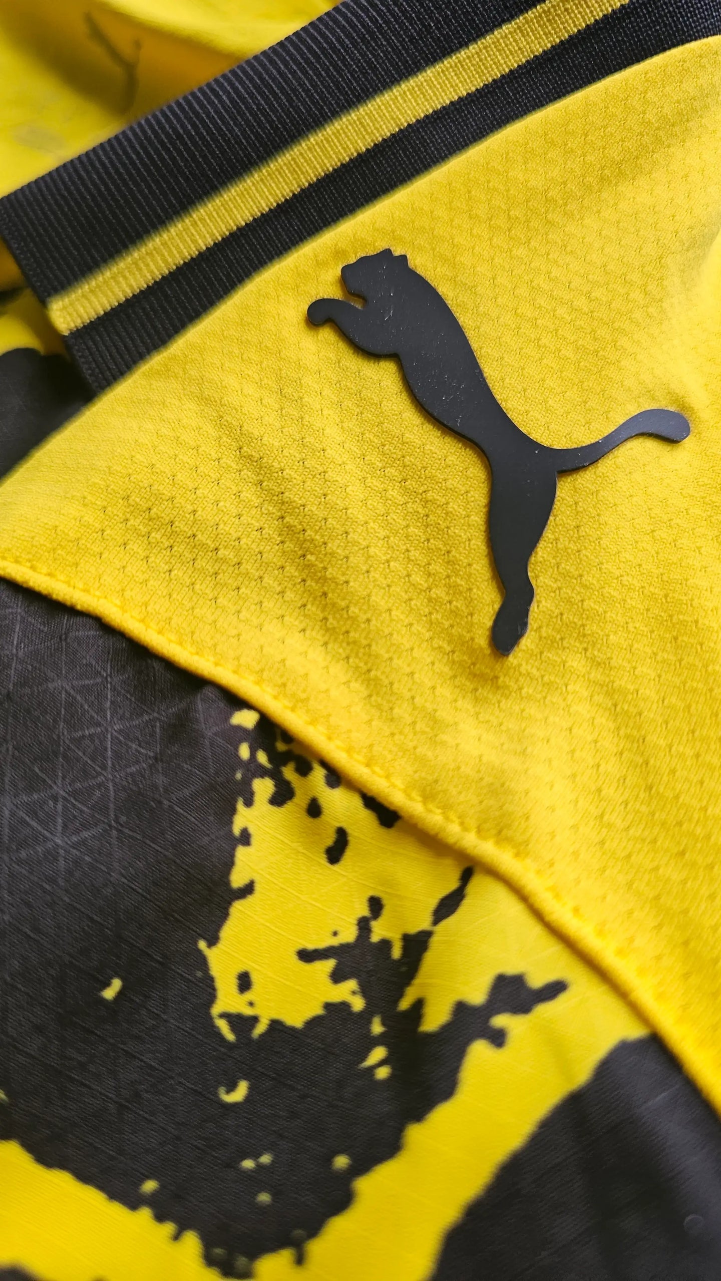 Close-up of Puma logo in black on yellow fabric, part of the Dortmund shirt design.