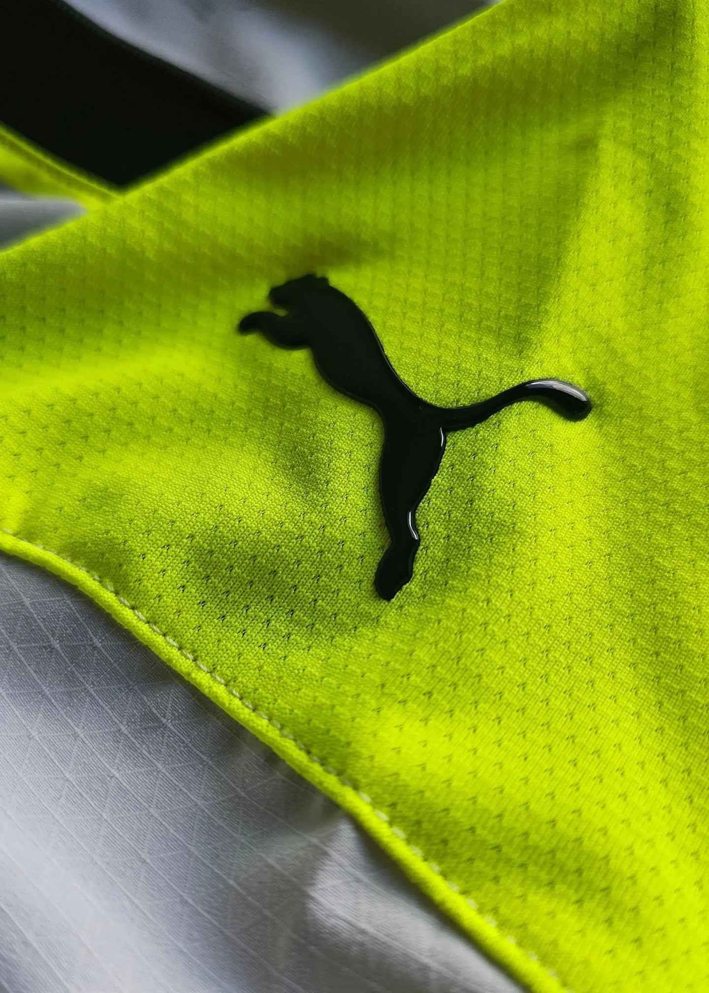 Close-up of the black Puma logo on the bright yellow fabric of the shirt.