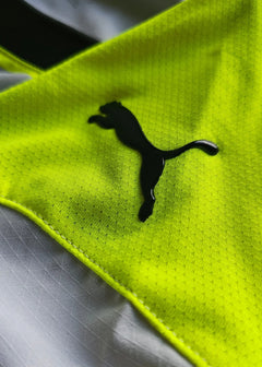 Close-up of the black Puma logo on the bright yellow fabric of the shirt.