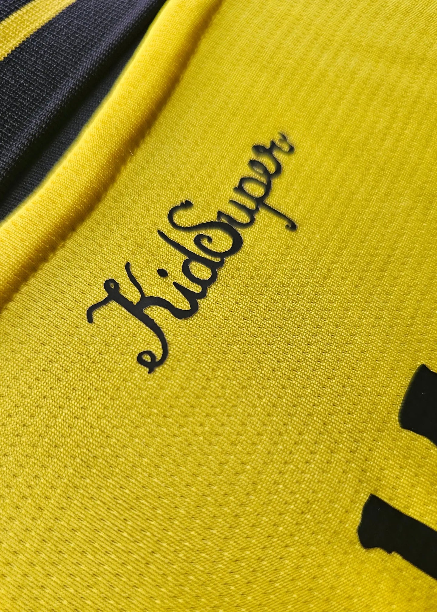 Detail view of the signed shirt featuring 'KidSuper' in black on a yellow background.