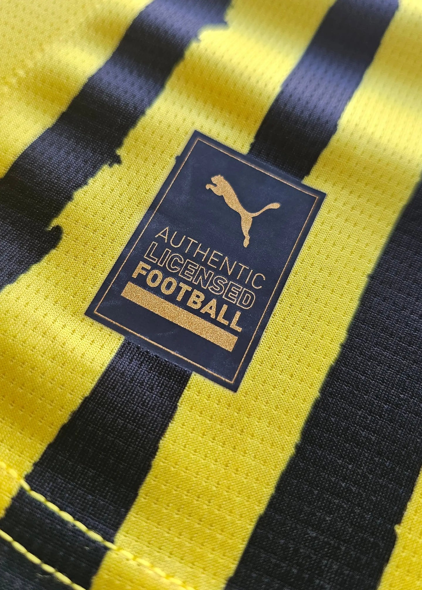 Close-up of the Puma label, reading AUTHENTIC LICENSED FOOTBALL on a yellow and black fabric.