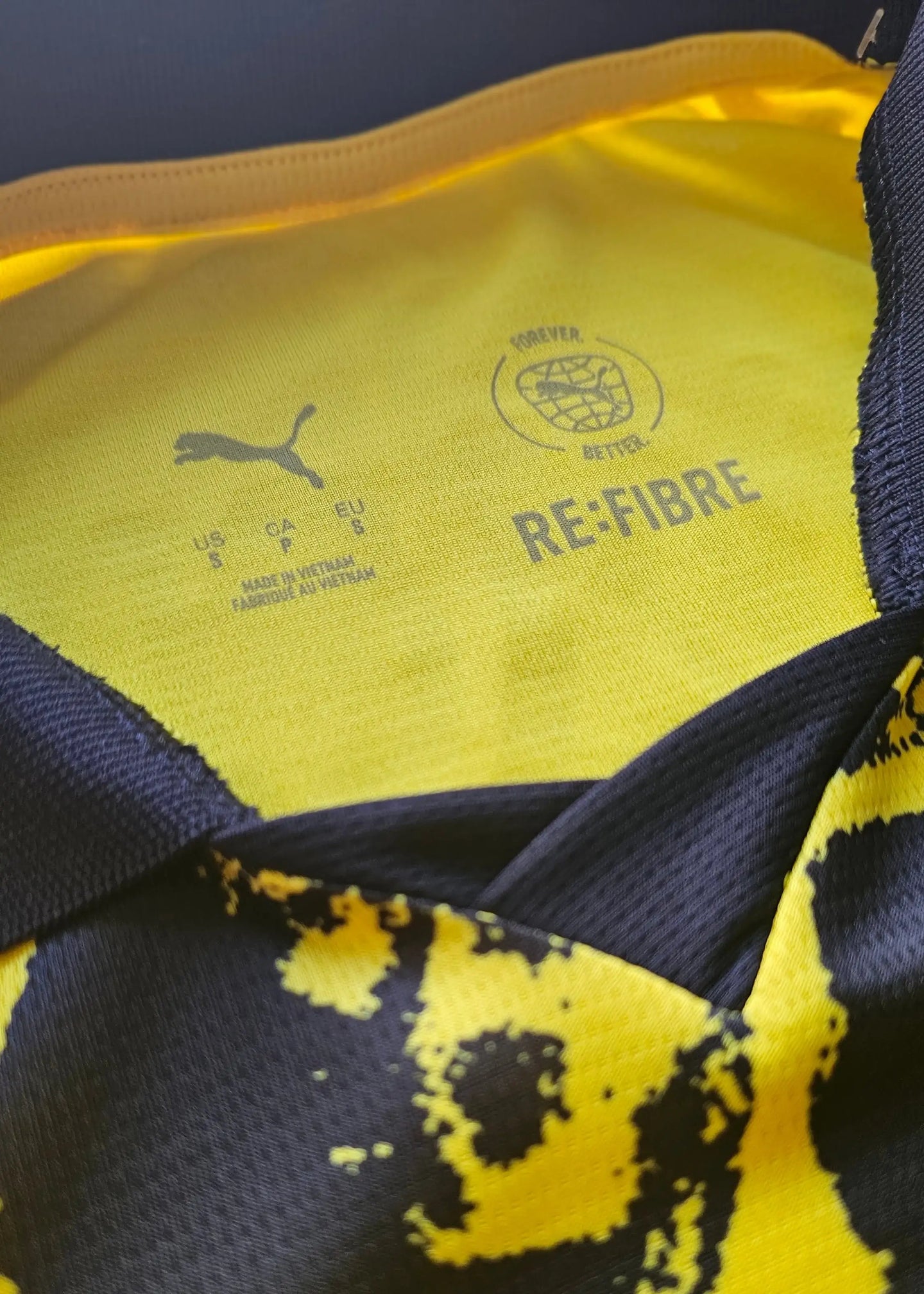Interior view showing Puma logo, care instructions, and RE:FIBRE text on a yellow and black football shirt.
