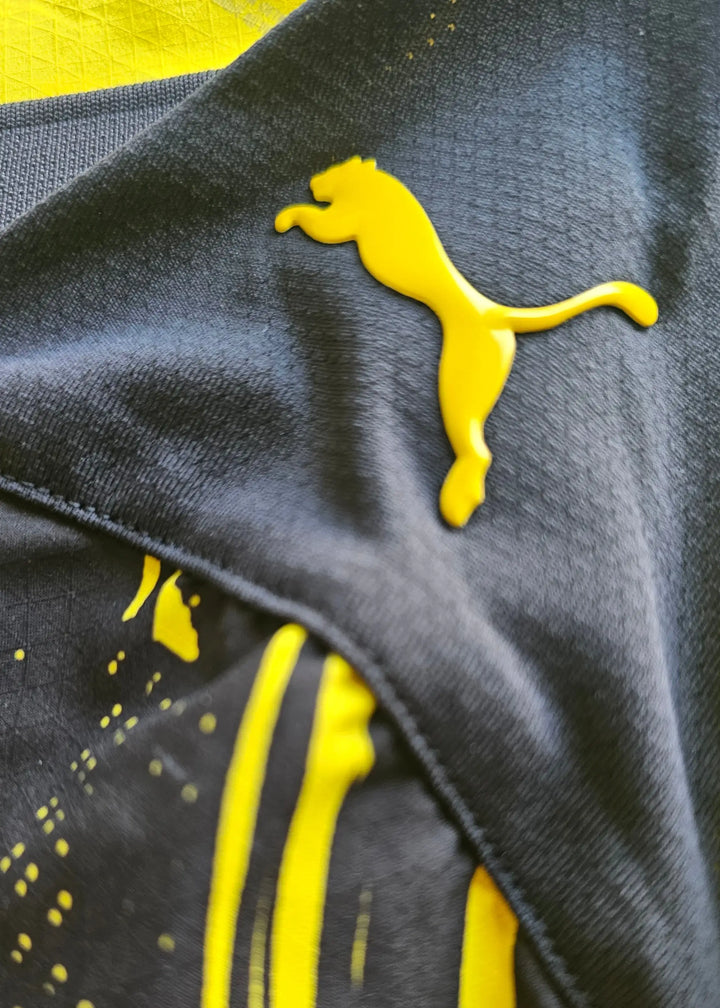 Close-up of yellow Puma logo on black fabric with yellow design details.