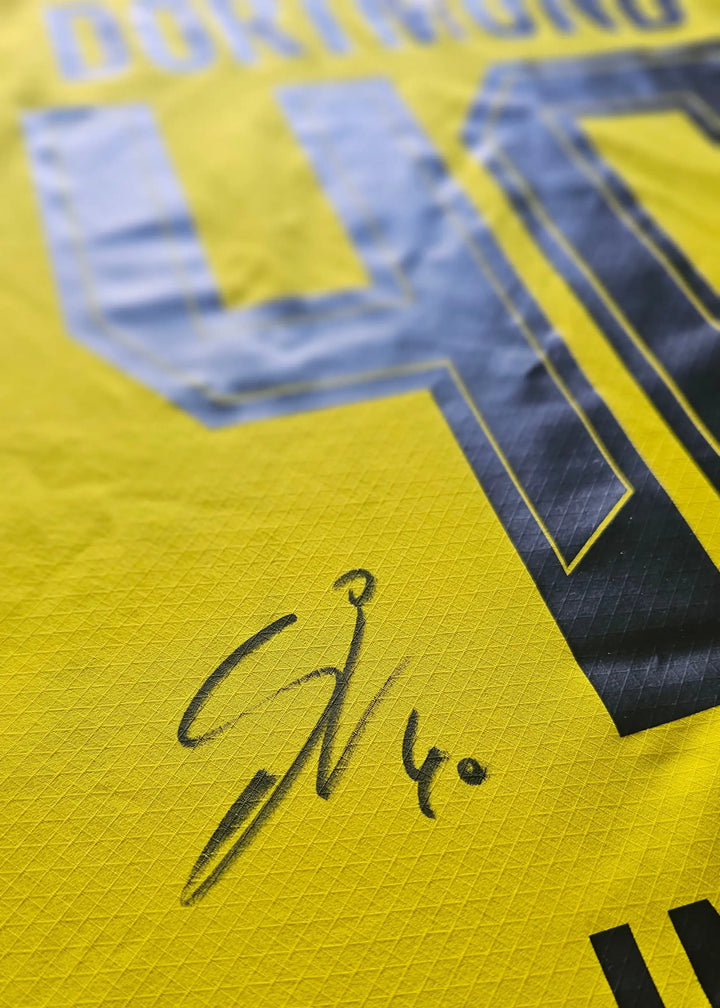 Detail view showing the signature of Samuele Inácio on a yellow Borussia Dortmund football shirt.