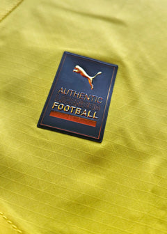 Close-up of the crest detail with 'AUTHENTIC LICENSED FOOTBALL' and Puma logo on yellow fabric.