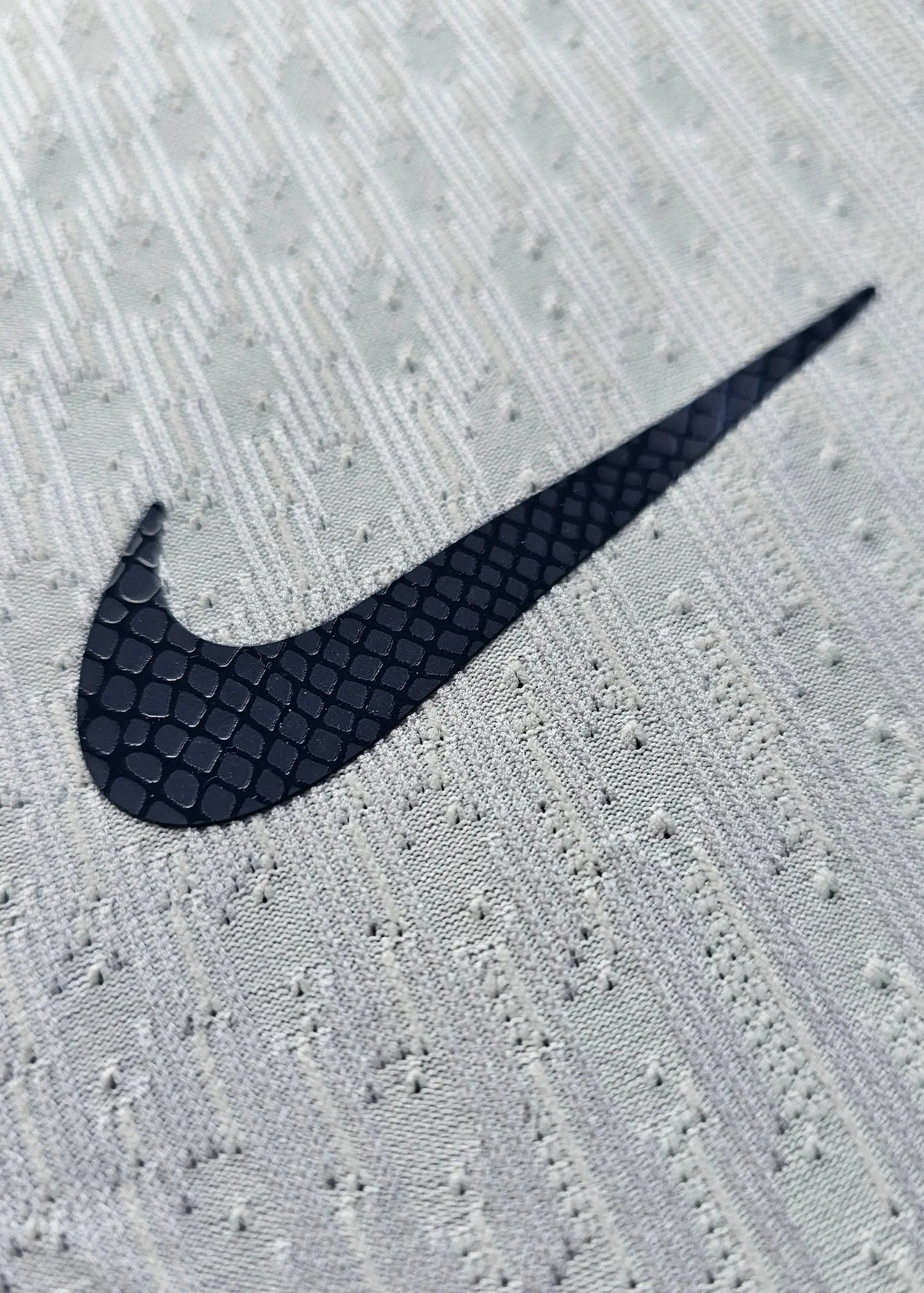 Close-up of the Nike logo on the away football shirt in white and navy colors.