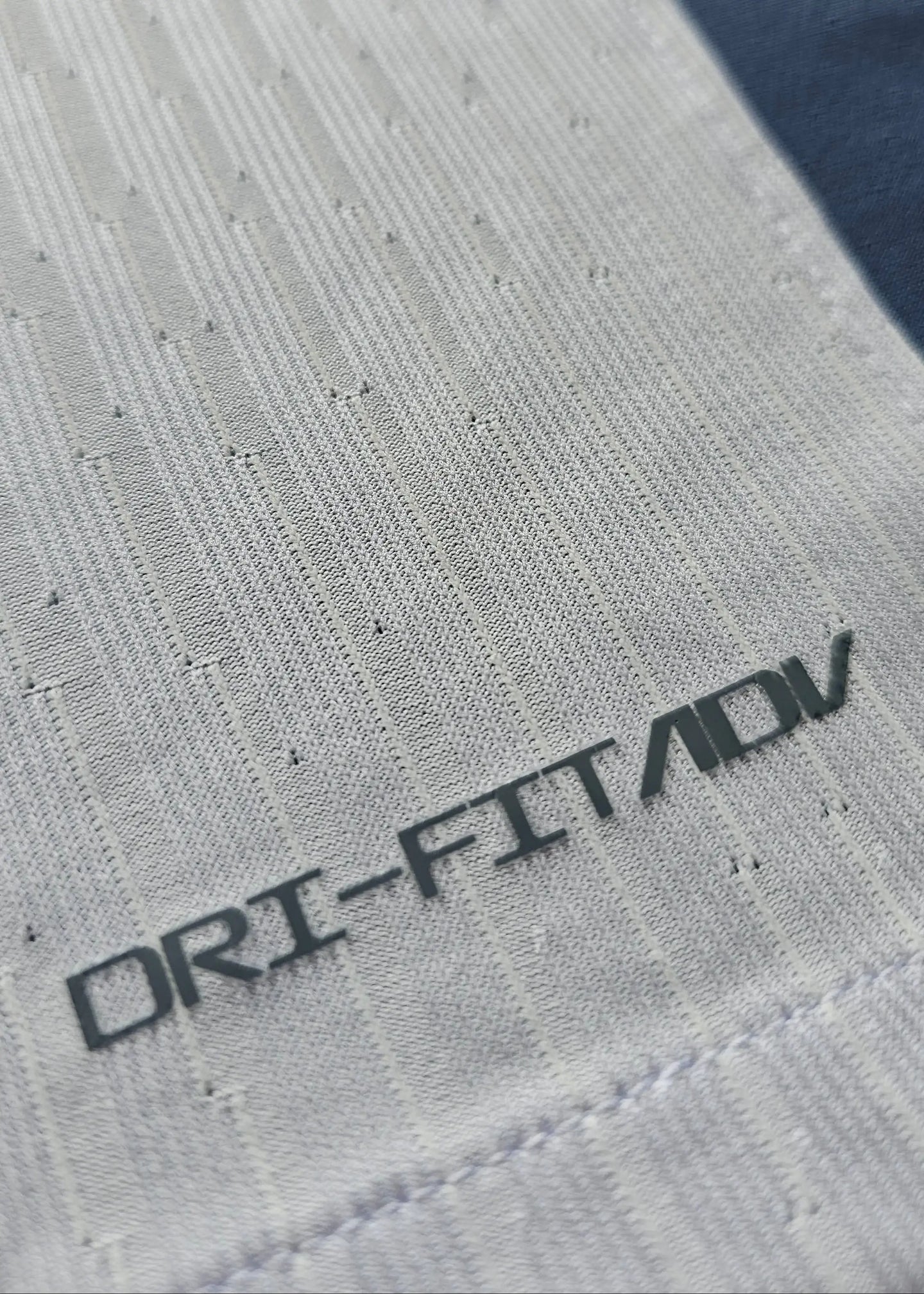 Close-up showing 'DRI-FIT ADV' text on the fabric of the white and navy football shirt.