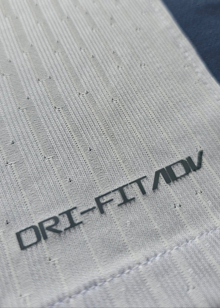 Close-up showing 'DRI-FIT ADV' text on the fabric of the white and navy football shirt.