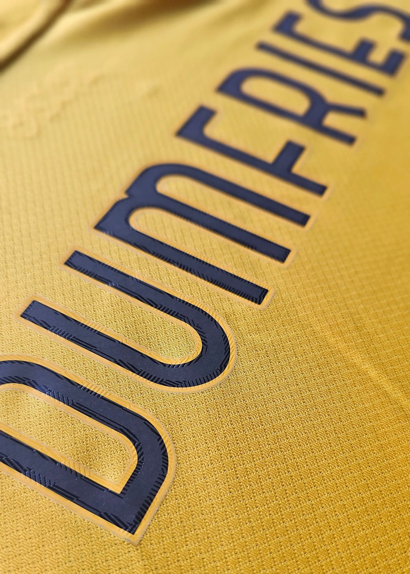 Close-up of DUMFRIES printed in black on a yellow football shirt.