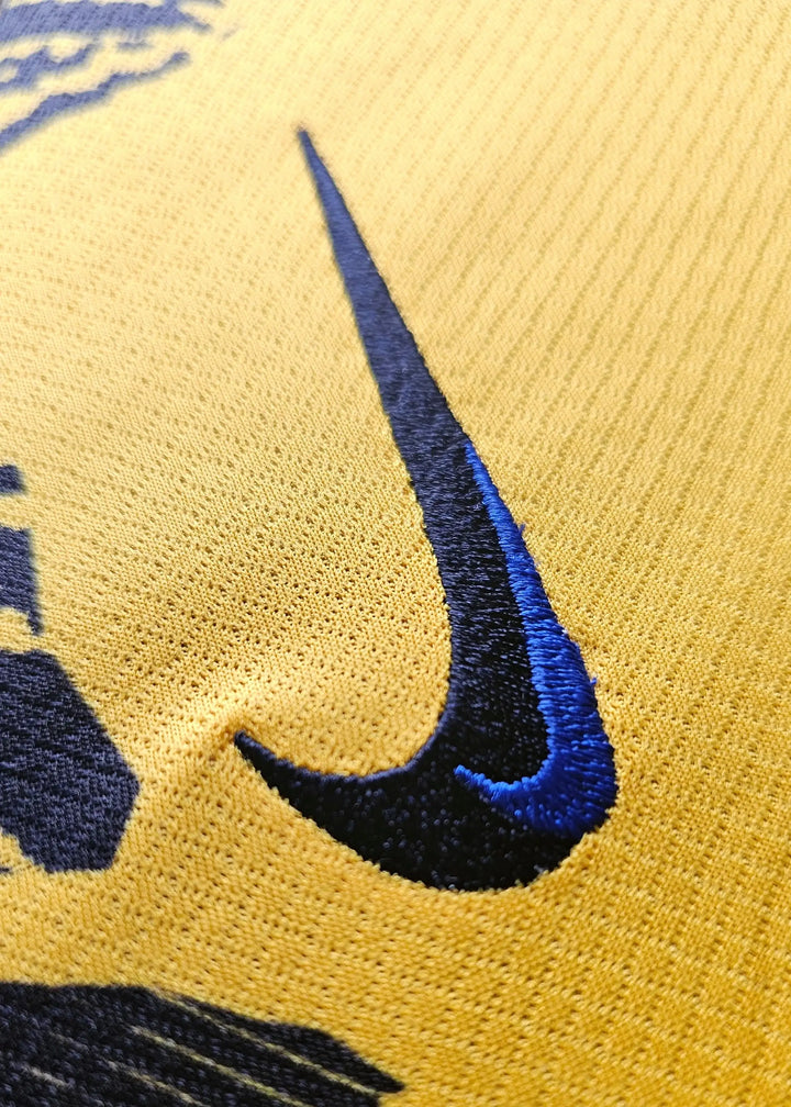 Close-up detail of the blue Nike logo stitched on a yellow football shirt.