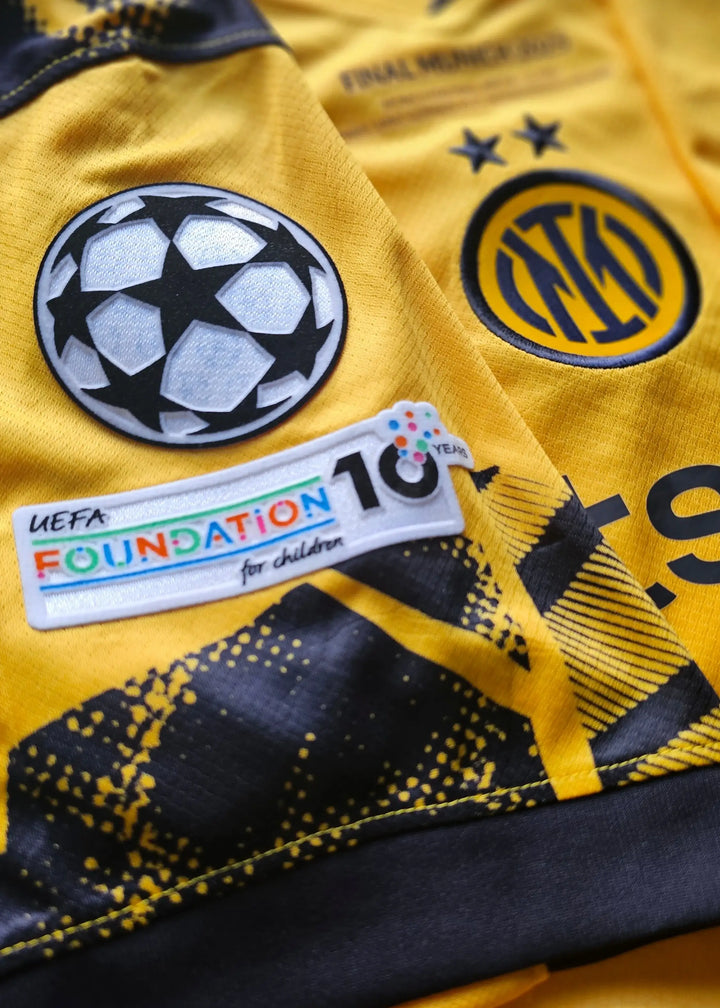 Detailed view showing UEFA Champions League logo, Inter Milan crest, and Foundation patch on a yellow football shirt.