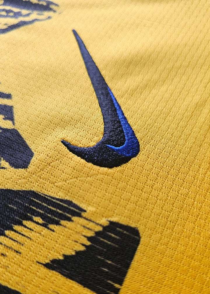 Close-up showing the black Nike logo on a yellow football shirt.