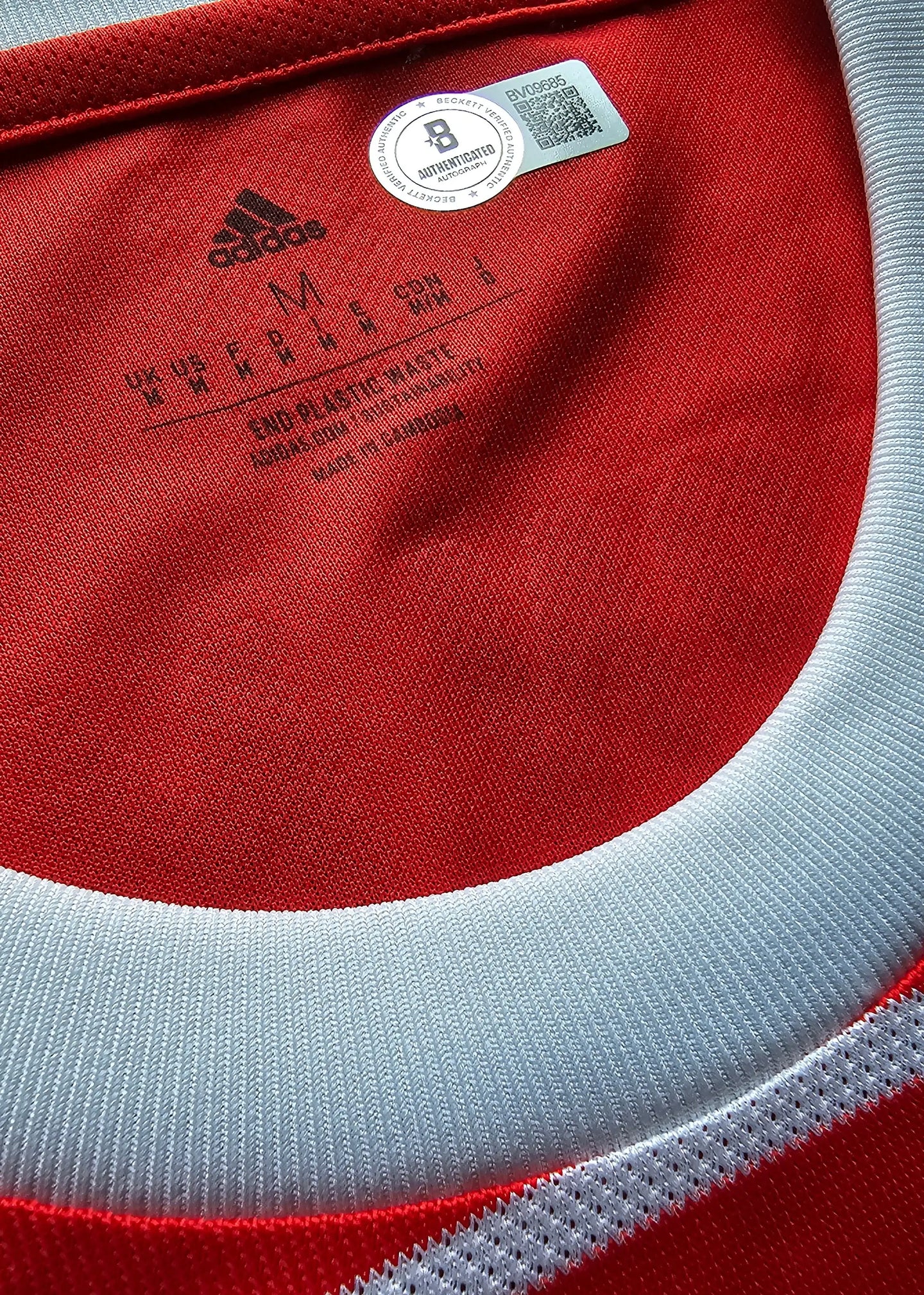 Close-up of a red and white sports jersey with Adidas logo and label.