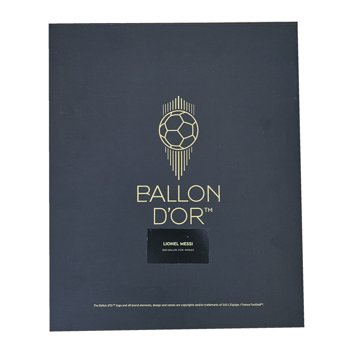 Lid of the Ballon d'Or presentation box, gold ball emblem above the Lionel Messi name plaque, boxed signed Barcelona shirt.