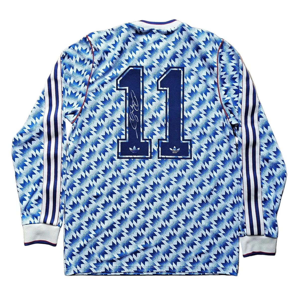 A long-sleeve soccer jersey with a blue and white geometric pattern, featuring the number 11 on the back and three stripes on the sleeves, laid flat on a wooden floor.