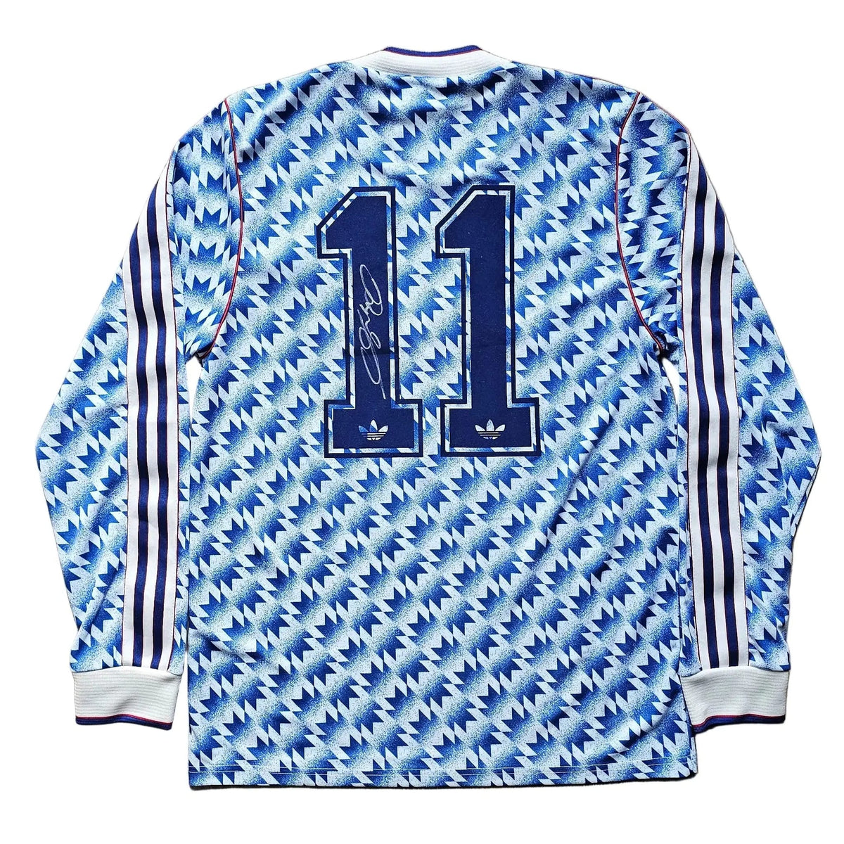 A long-sleeve soccer jersey with the number 11 printed on the back, laid flat on a light brown wooden floor. The jersey features a blue and white patterned design with three stripes on the sleeves.