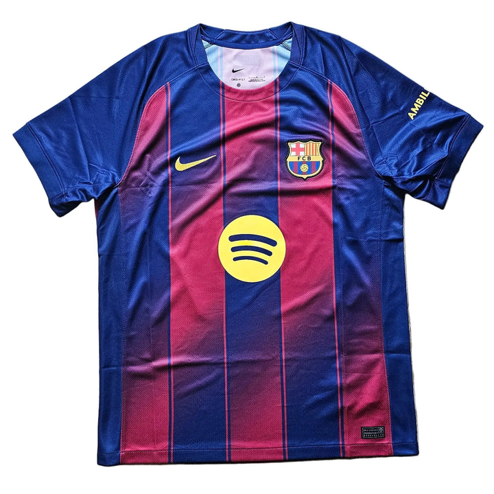 A Nike FC Barcelona home soccer jersey with blue and magenta vertical stripes, featuring the yellow Spotify sponsor logo on the front, laid flat on a light wood floor.