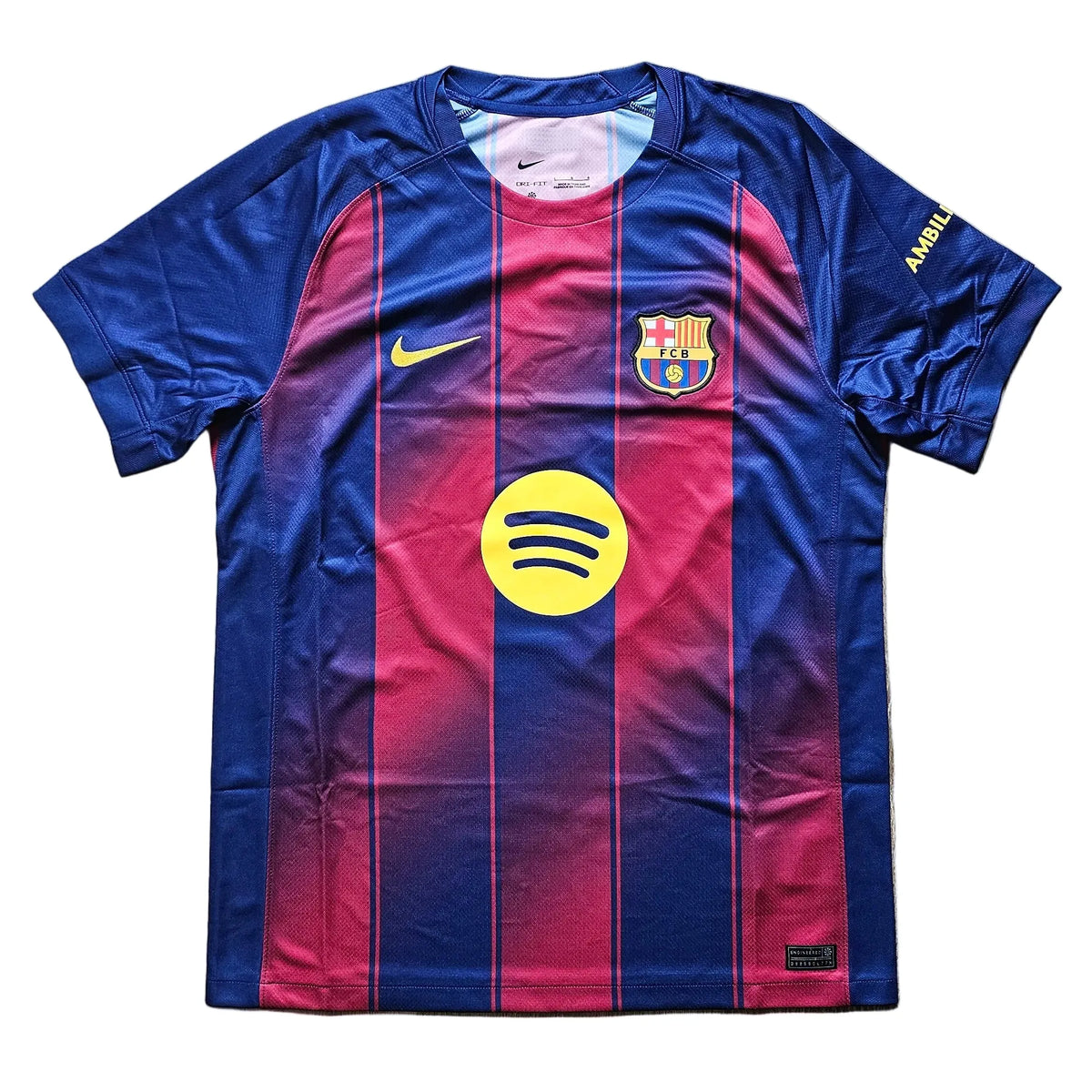 A Nike FC Barcelona home soccer jersey with a blue and red gradient design, featuring the yellow Spotify sponsor logo on the front, laid flat on a light wood floor.