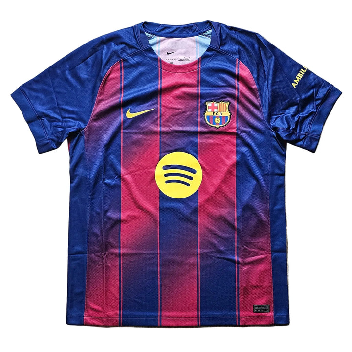 A Nike FC Barcelona home soccer jersey with a blue and red gradient design, featuring the yellow Spotify sponsor logo on the front, laid flat on a light wood floor.