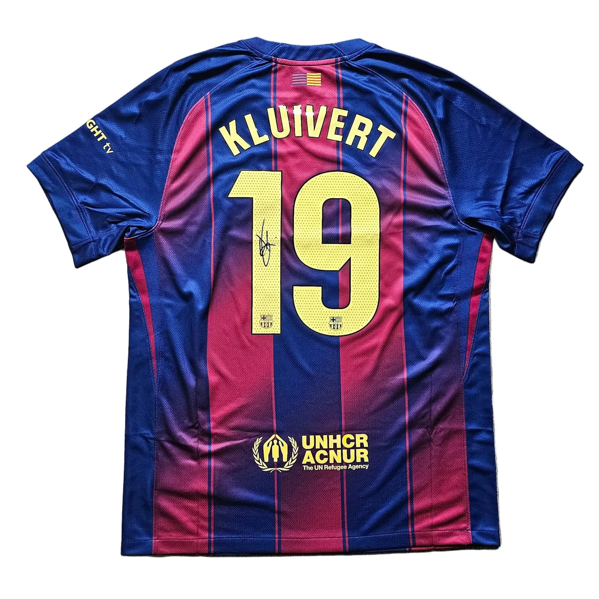 A FC Barcelona home soccer jersey with the back view, featuring 'KLUIVERT' and the number '19' in yellow, laid flat on a light wood floor.