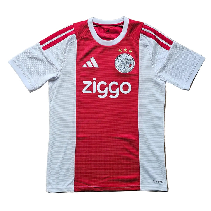 A red and white short-sleeve soccer jersey laid flat on a wooden floor. The jersey features a vertical red stripe down the center, white side panels and sleeves, red shoulder stripes, the Adidas logo on the right chest, a circular club crest on the left chest, and 'ziggo' sponsor text across the front.