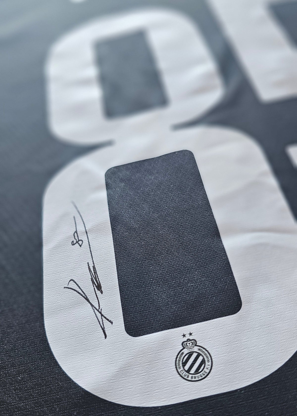 Signed black Club Brugge 2026-27 home shirt, close-up of Tian Nai Koren's signature on the 8 of the white number 85