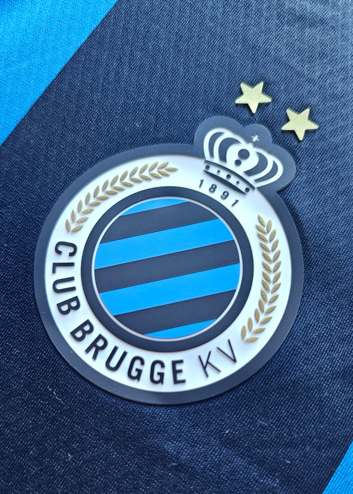 Club Brugge KV crest with crown and two gold stars on the black and blue Tian Nai Koren 2026-27 home shirt, number 85