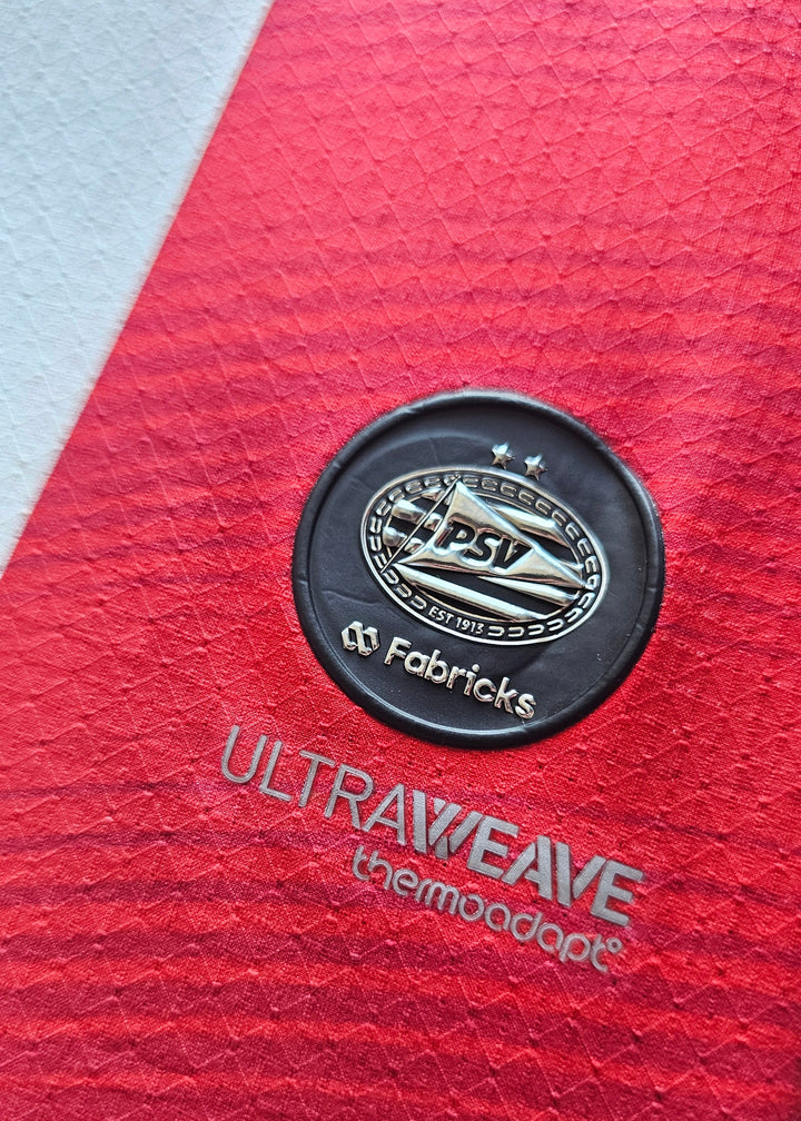 Fabricks badge with a silver PSV crest above the Ultraweave thermoadapt print on the Amir Bouhamdi PSV 2026-27 home shirt