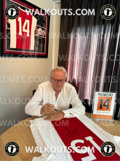 Arie Haan signing a red and white Ajax jersey with No. 15 and a visible signature.