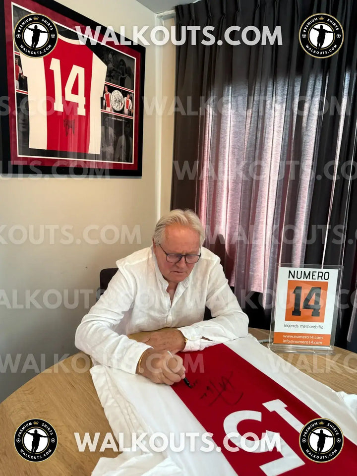 Arie Haan signing a red and white soccer jersey with No. 25, displaying his signature prominently.
