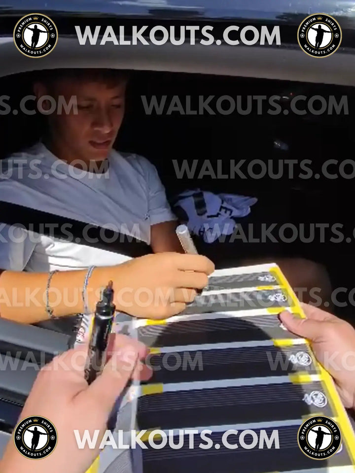 Arda Güler signs a Real Madrid 24 football shirt while seated in a vehicle.