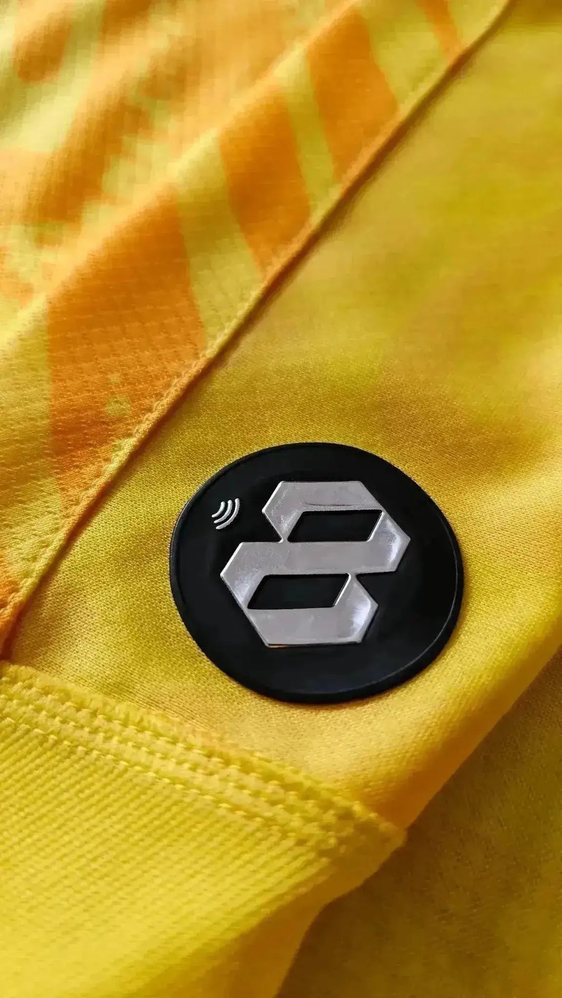 Close-up of the black and silver '8' logo detail on the yellow football shirt.