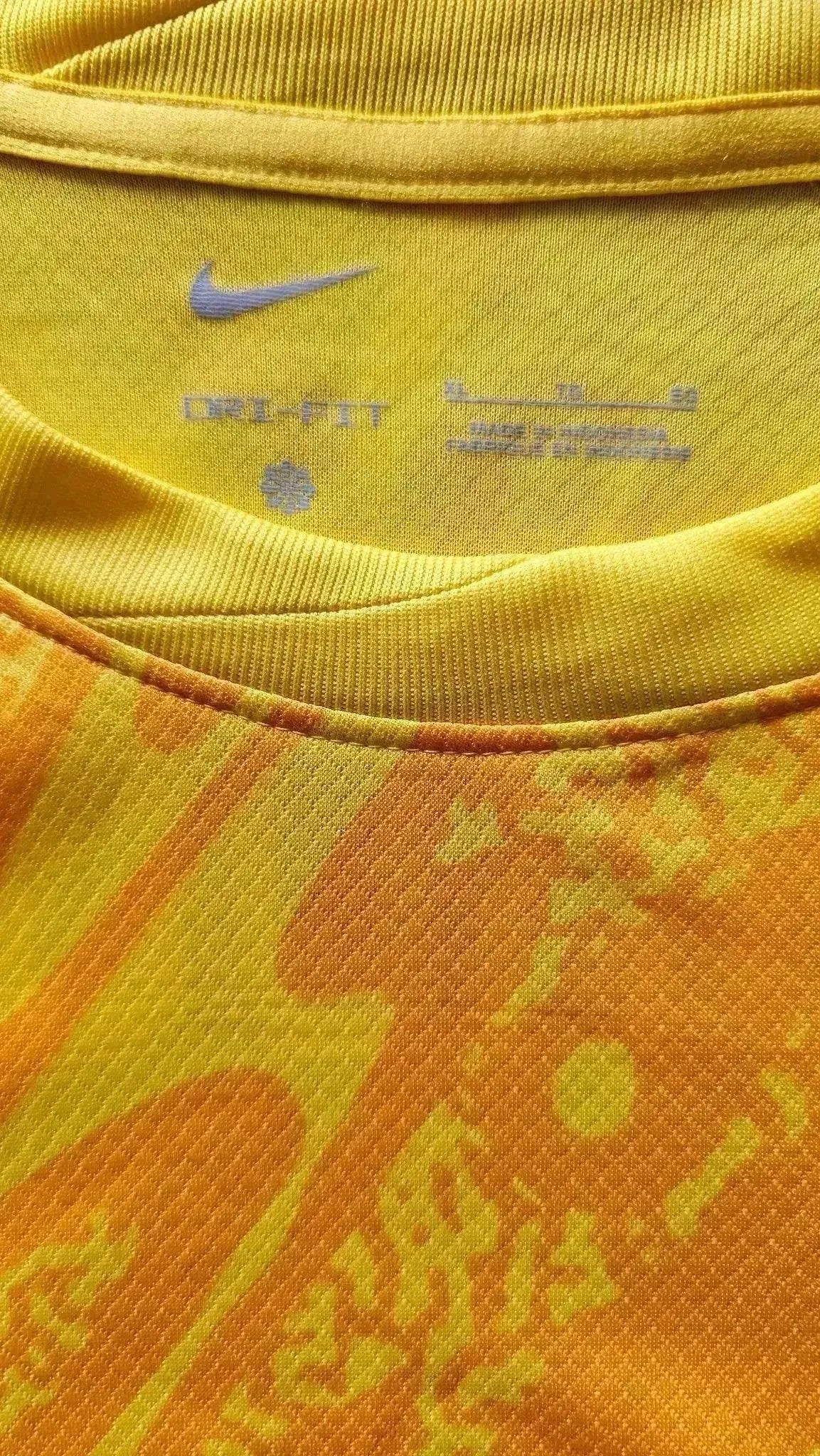 Nike logo and care label detail on a yellow football shirt featuring orange accents.