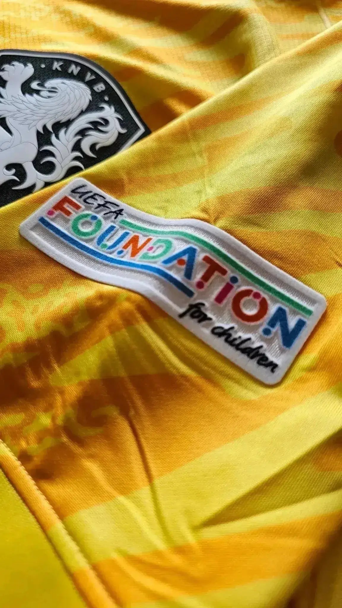 Crest detail featuring KNVB logo and UEFA Foundation for children patch on yellow football shirt.