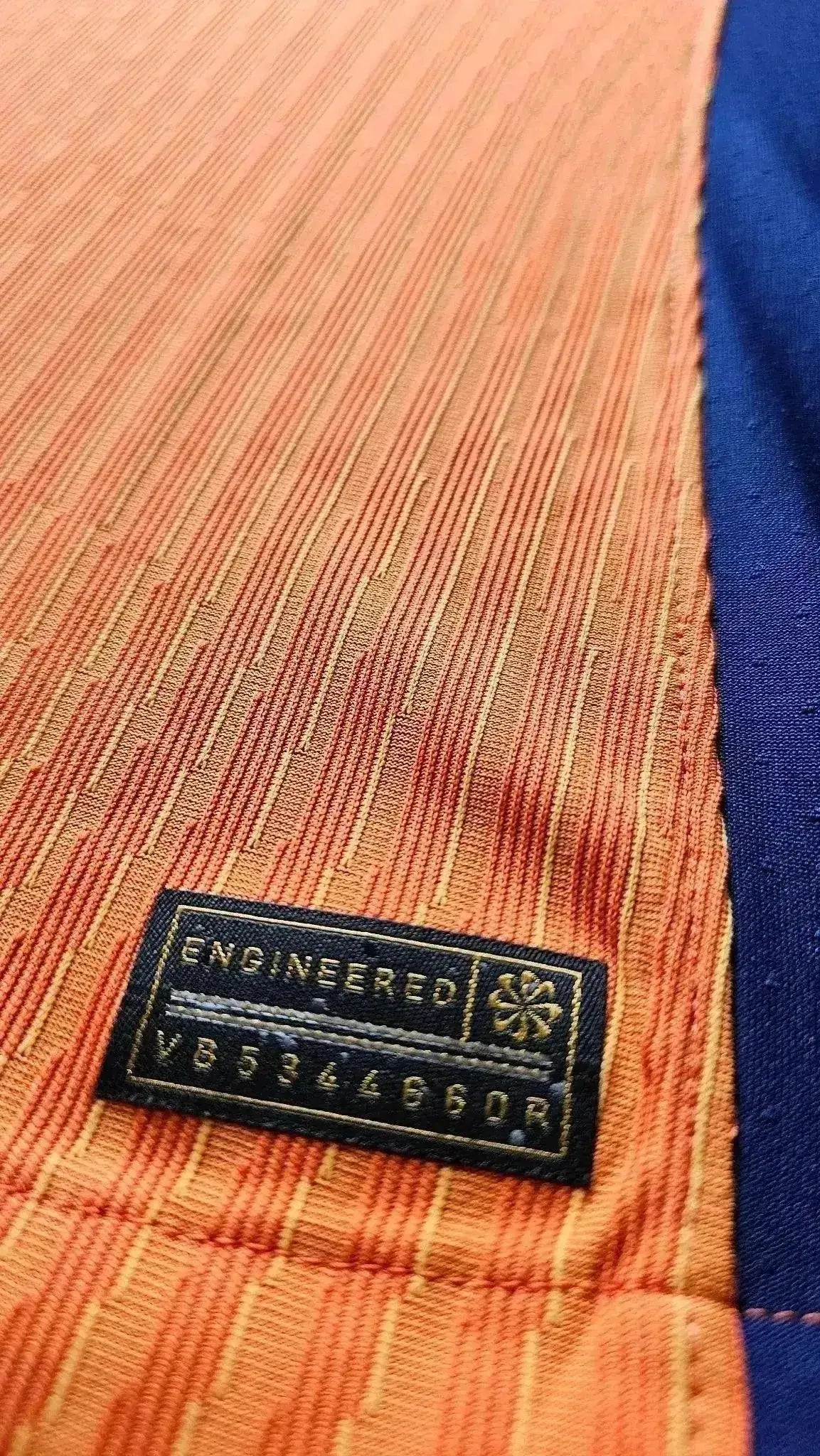 Close-up of the label showing 'ENGINEERED' and code 'VB594496G0R' on the orange and blue football shirt.