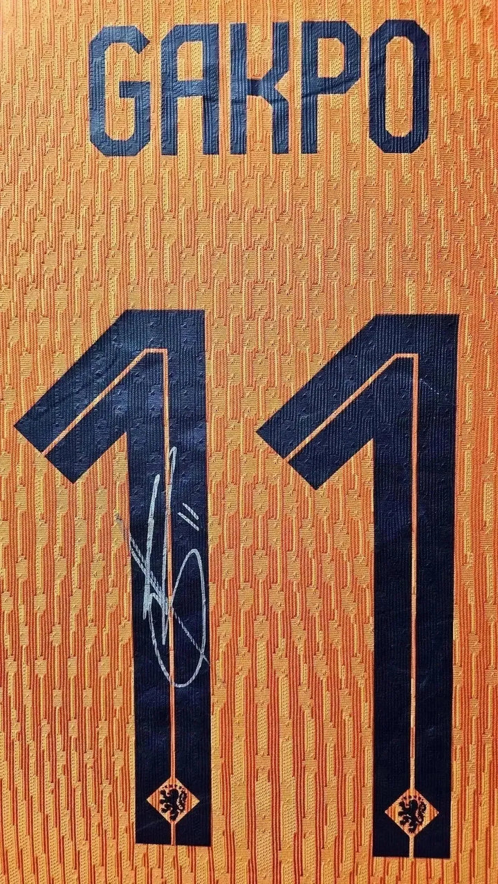 Detail view of orange football shirt with GAKPO and No. 11, featuring a signature.