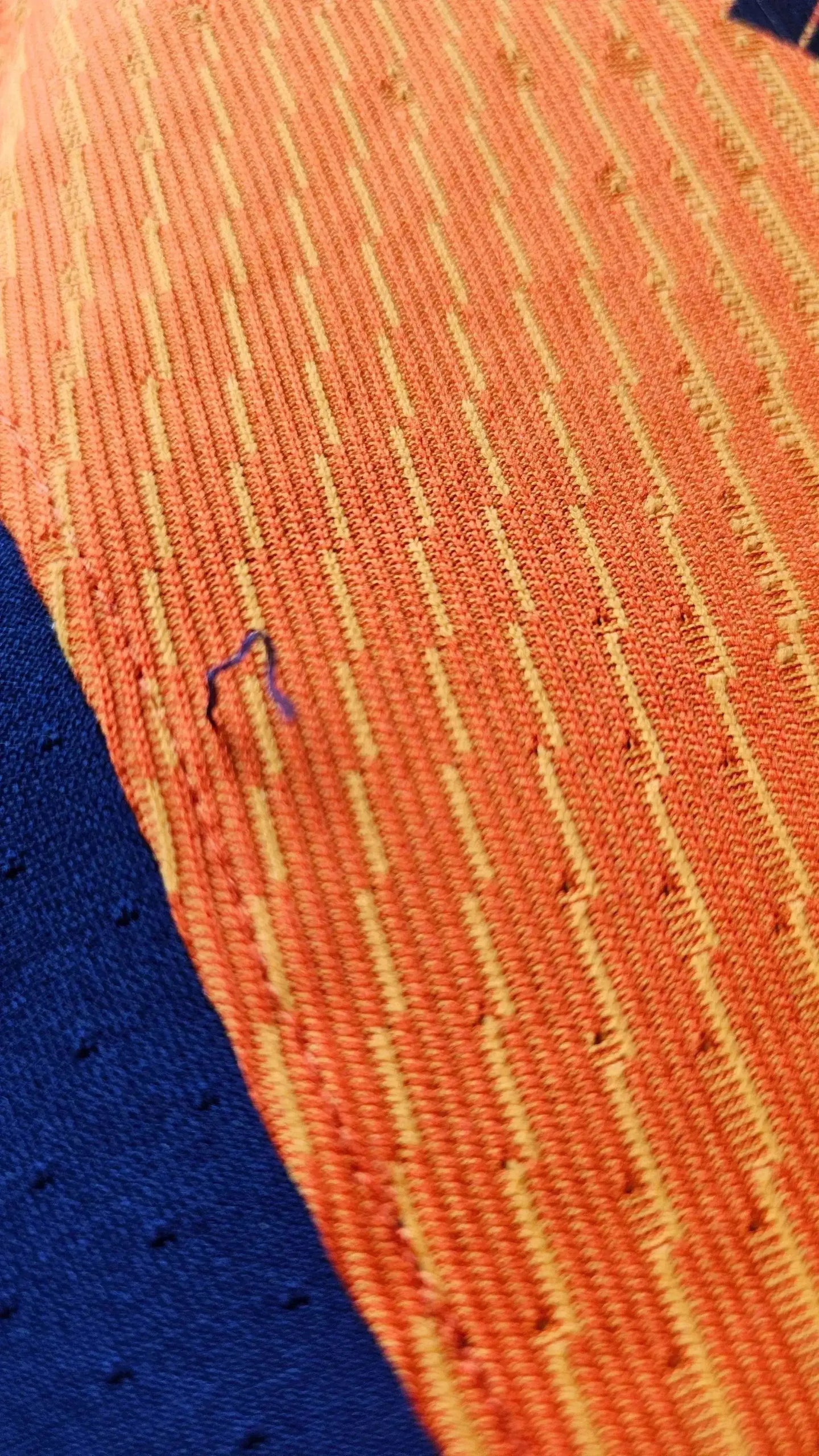 Close-up of orange and blue fabric showcasing stitching details and a loose thread.