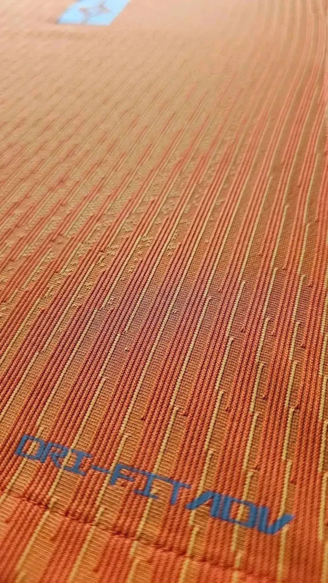 Close-up of orange fabric showing 'DRI-FIT ADV' text and textured detail.
