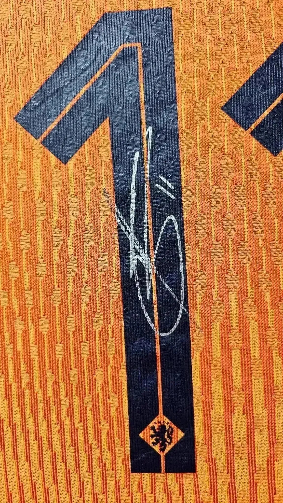 Detail showing No. 1 and signature on an orange football shirt with lion emblem.