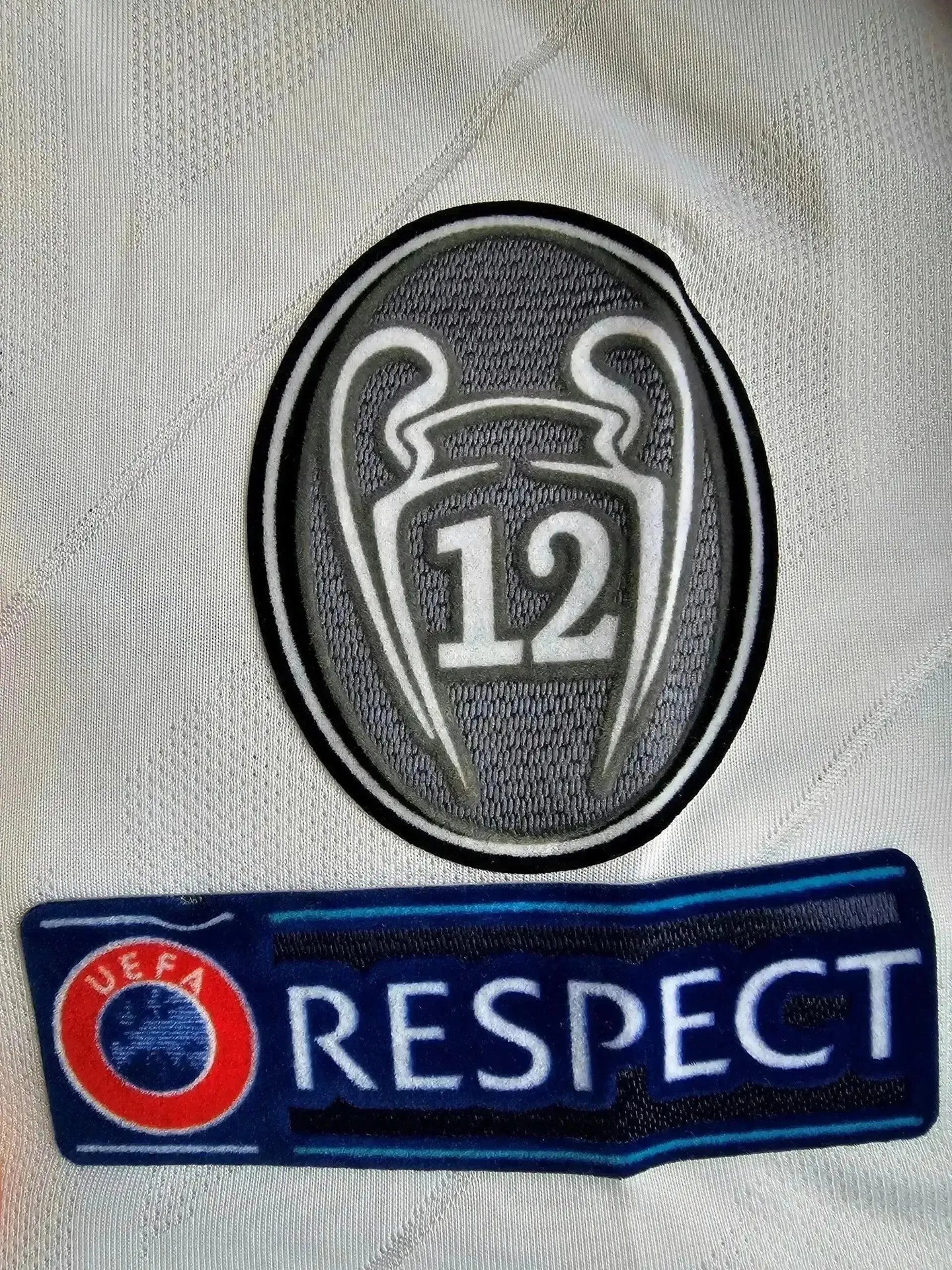 Detail showing UEFA Champions League badge with '12' and Respect logo on the shirt.