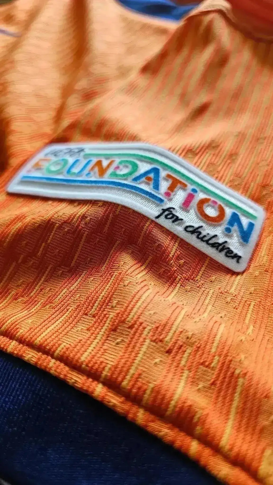 Crest detail showing colorful 'FOUNDATION for children' logo on orange fabric.