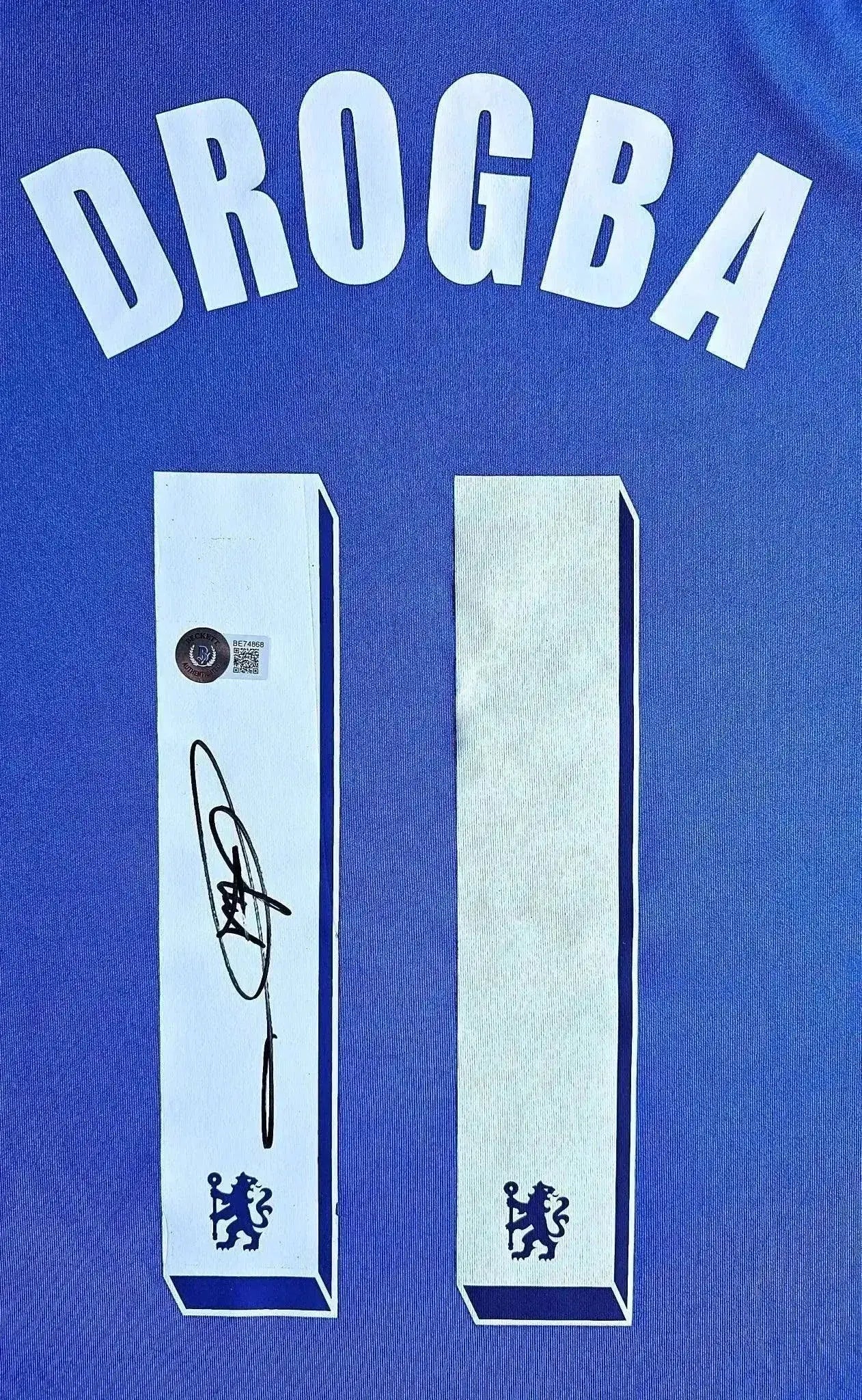 Back view showing Drogba, No. 11, and authentic signature on blue Chelsea soccer jersey.