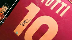 View showing signature of Totti above No. 10 on AS Roma shirt in red and yellow.