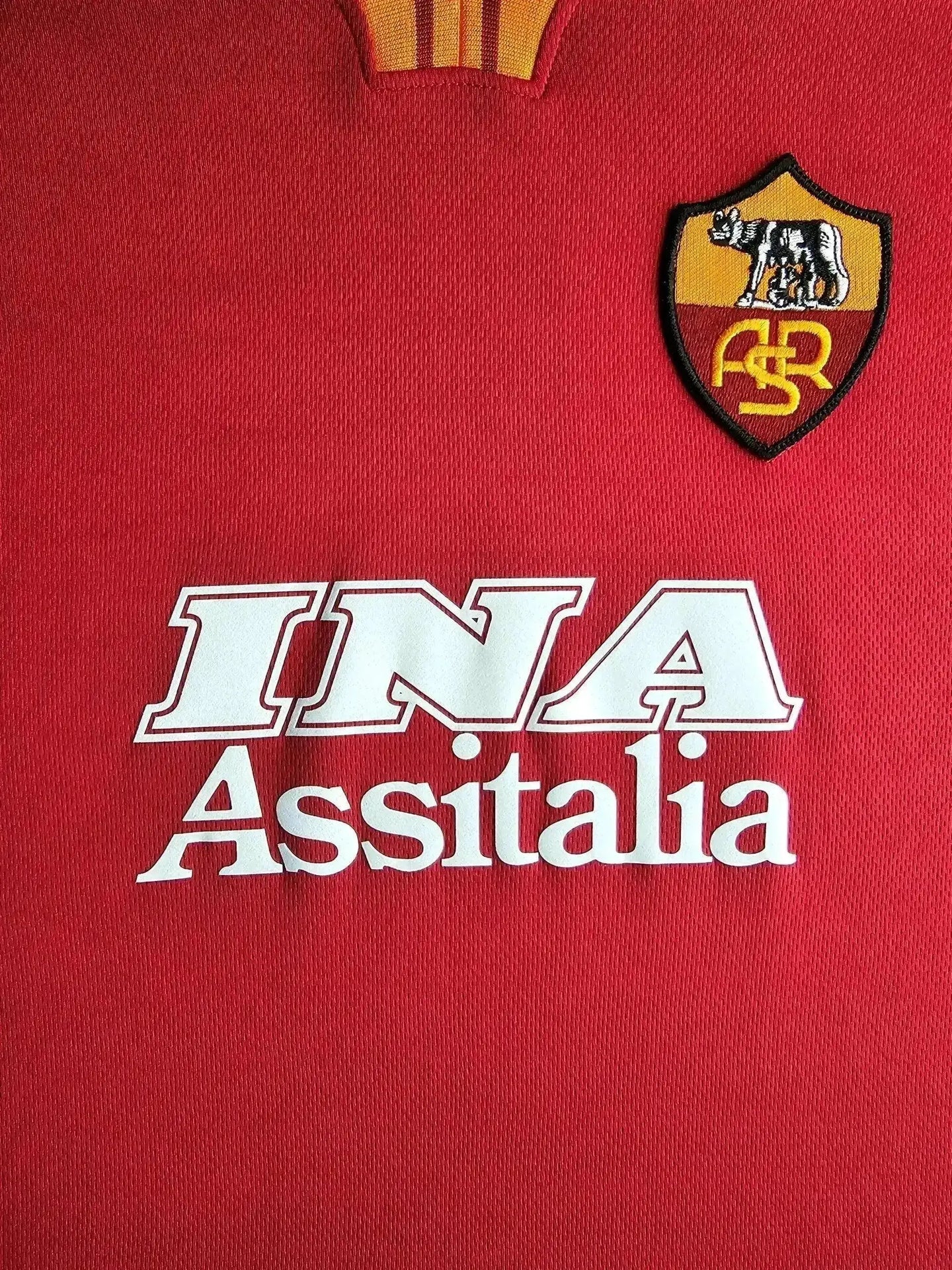 Detail view showing A.S. Roma crest and INA Assitalia sponsor on red soccer jersey.