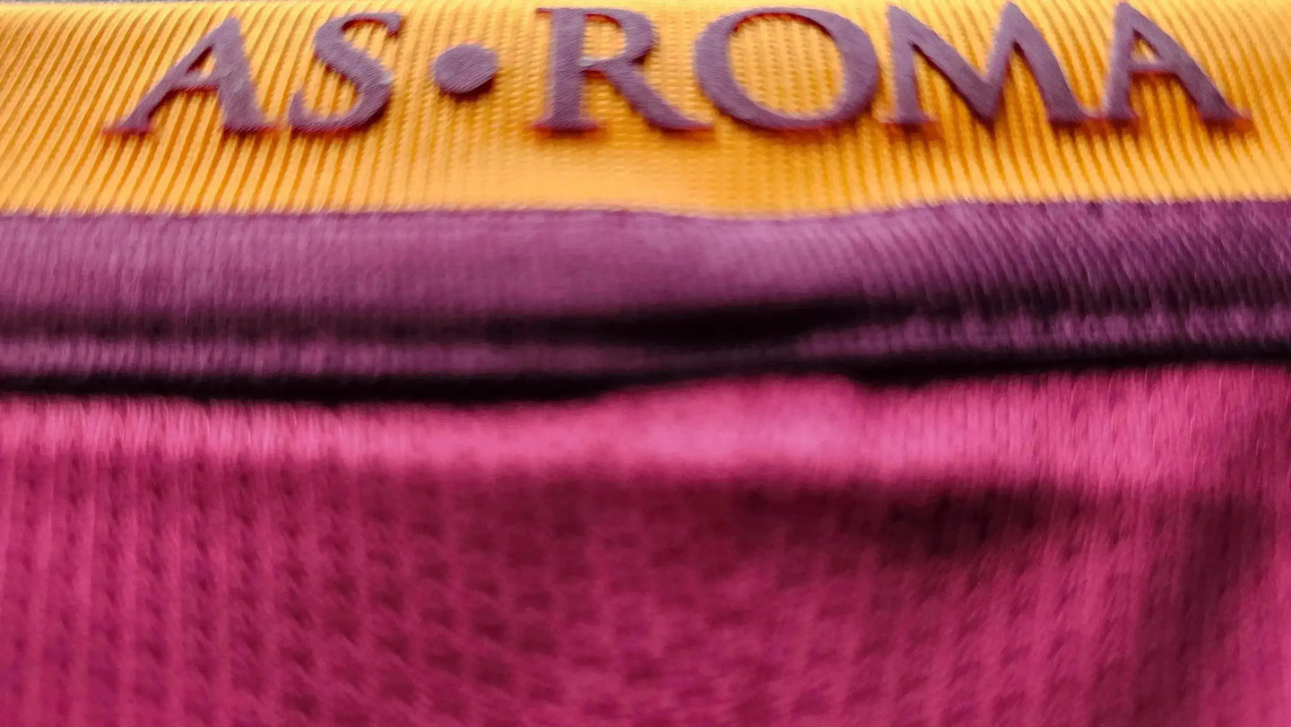 Close-up view of the AS Roma crest on the collar of a football shirt in red and yellow.