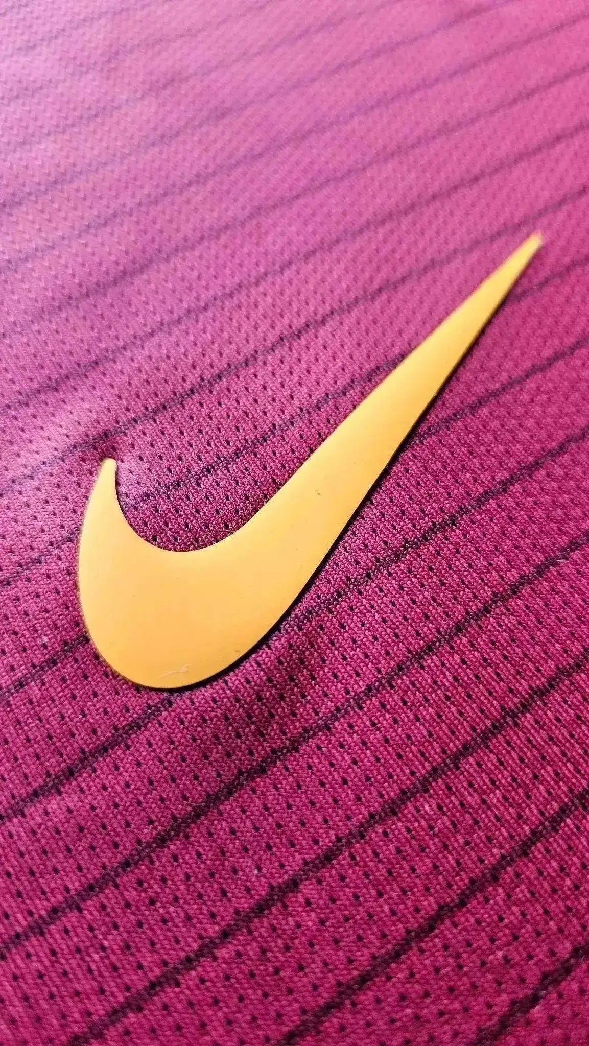 Close-up of Nike logo in orange on red football shirt fabric with textured pattern.